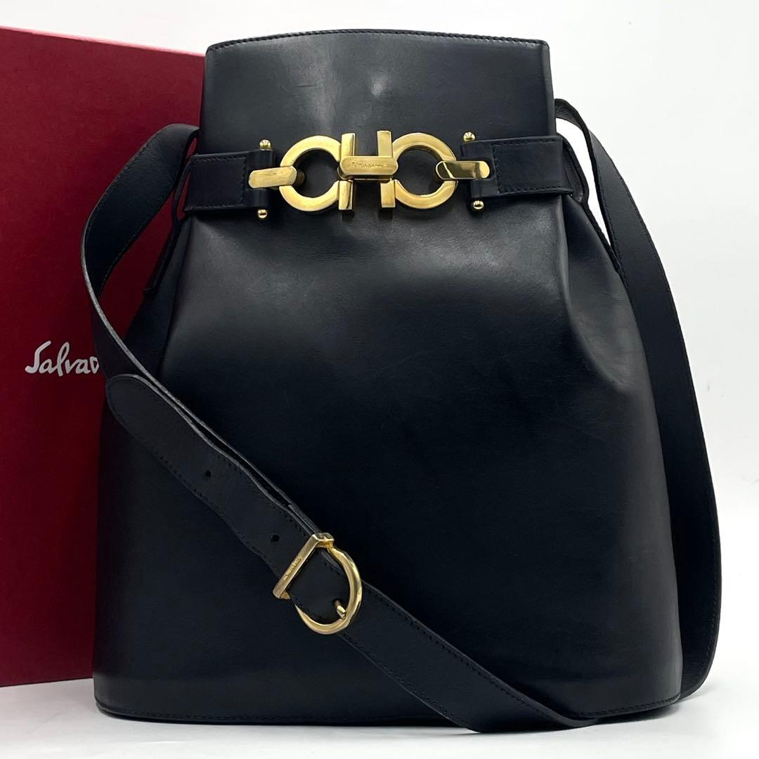 Front view of the black leather bucket bag with gold clasp and its box