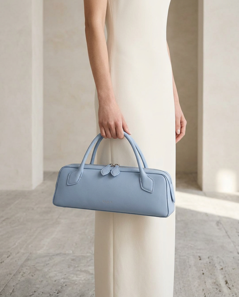 Model in an ivory dress carrying the powder-blue east-west top-handle bag